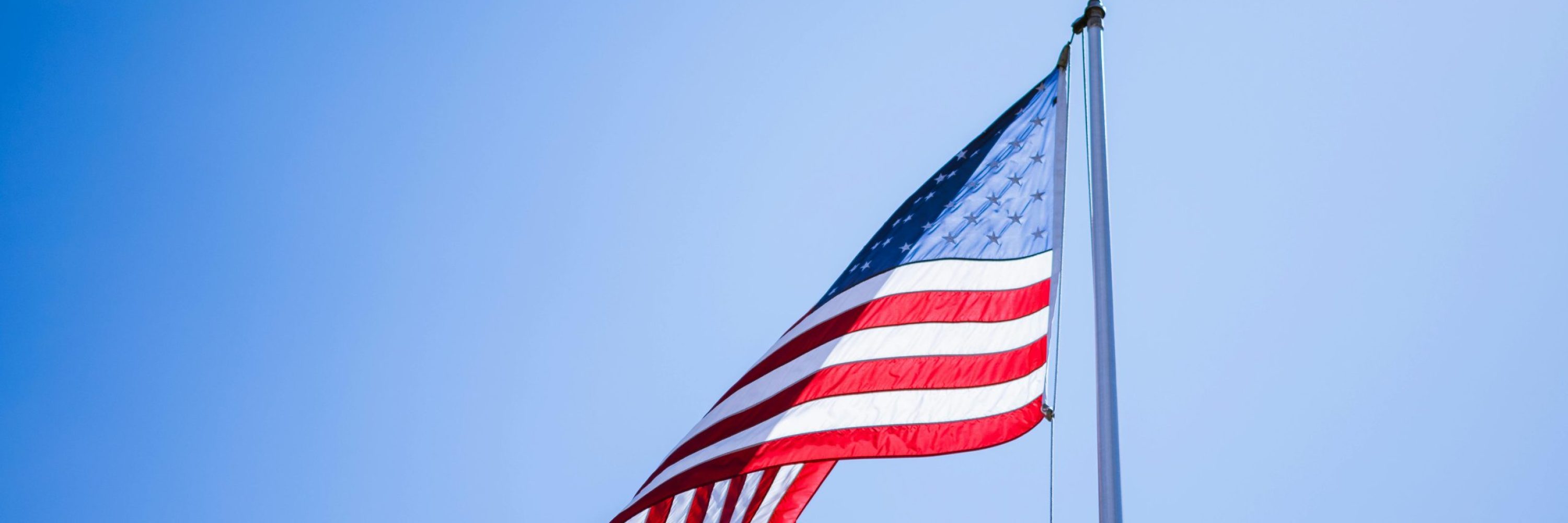 A vibrant American flag waves proudly on a tall flagpole against a clear blue sky.